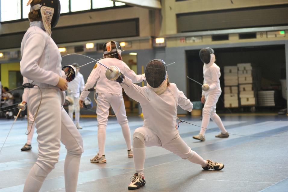 Training von Jugendlichen im Fechten, alle in weißer Ausrüstung, während ein Kämpfer eine Attacke ausführt.