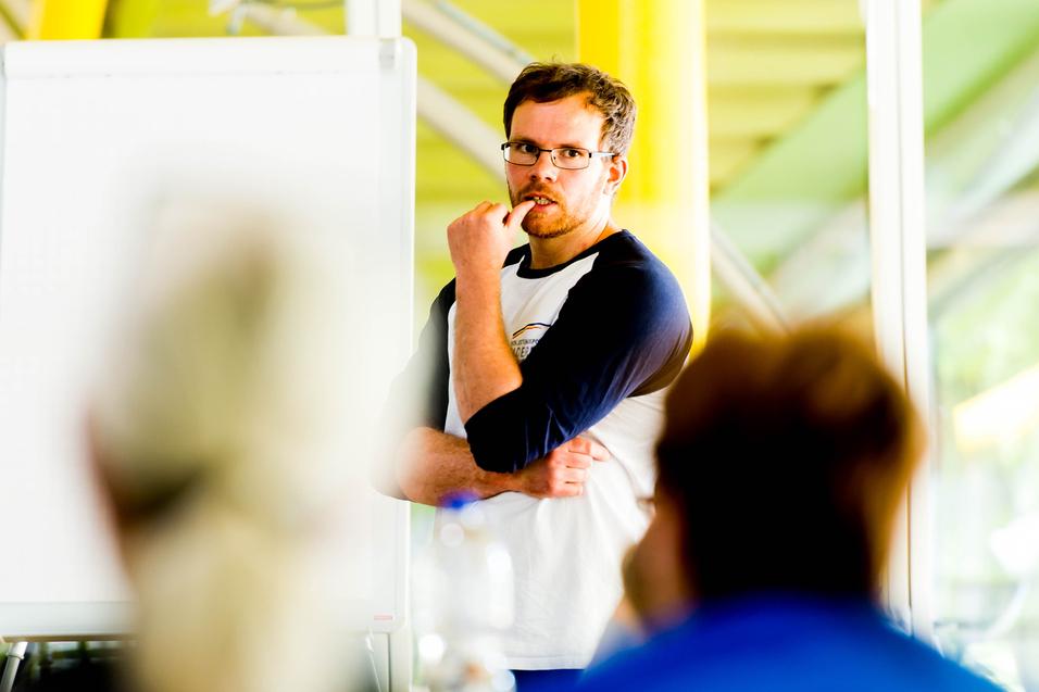 Mann mit Brille spricht vor einer Gruppe, ein Flipchart ist im Hintergrund sichtbar.