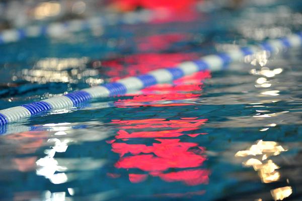 Reflektion einer blauen und weißen Schwimmbahn in klarem Wasser mit unscharfen Lichtern im Hintergrund.